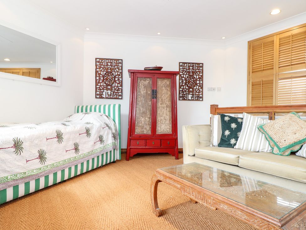A room with a striped bedspread a red cabinet a sofa with pillows and a glass coffee table at The Hexagon House in Goldsithney