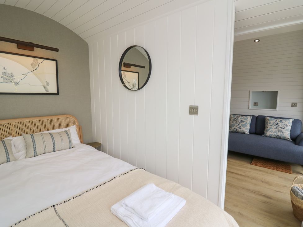 A bedroom with a bed and a round mirror on the wall next to a sitting area with a blue sofa at Ceunant in Llanfihangel-y-Creuddyn near Aberystwyth