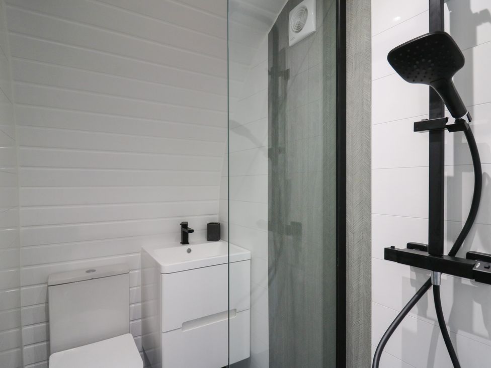A bathroom with a toilet, a sink with a black faucet, and a shower with a black showerhead at Ceunant in Llanfihangel-y-Creuddyn near Aberystwyth