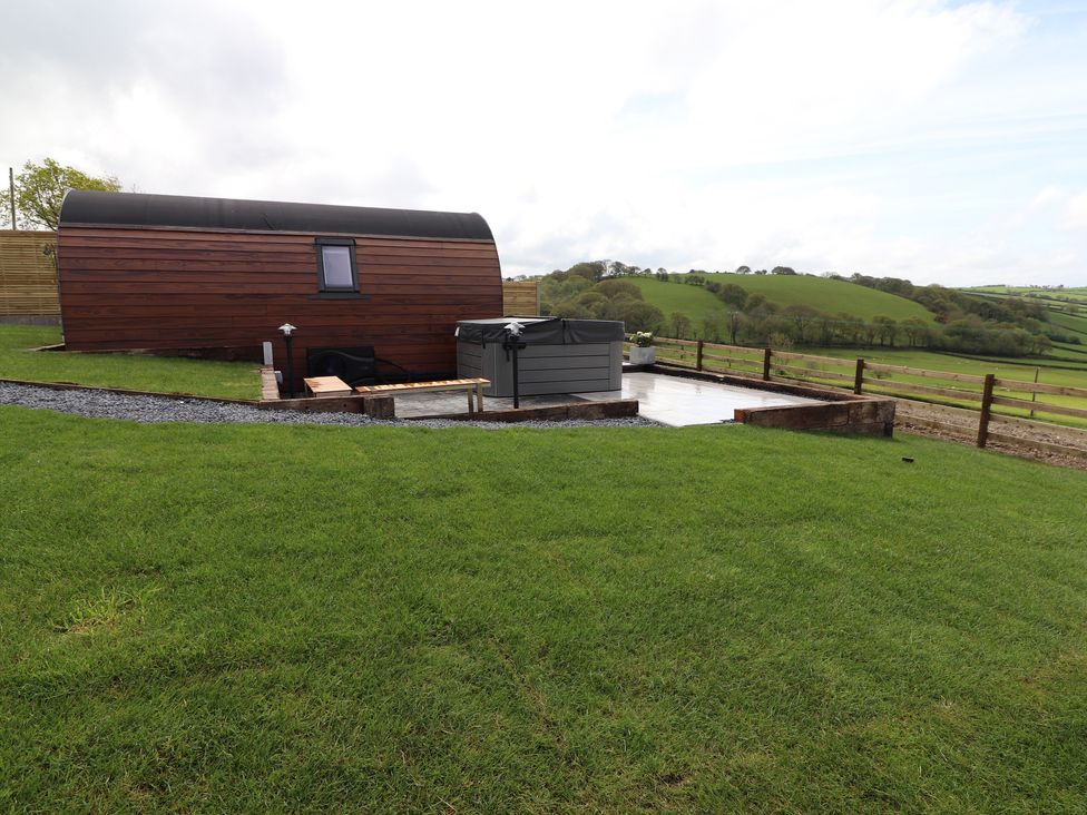 A small wooden cabin with a hot tub on a paved area surrounded by grass and wooden fences at Ceunant Llanfihangel-y-Creuddyn near Aberystwyth