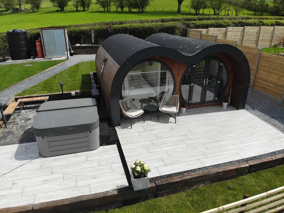 An outdoor patio area with two chairs and a table next to a cylindrical building and a covered hot tub at Ceunant Llanfihangel-y-Creuddyn near Aberystwyth
