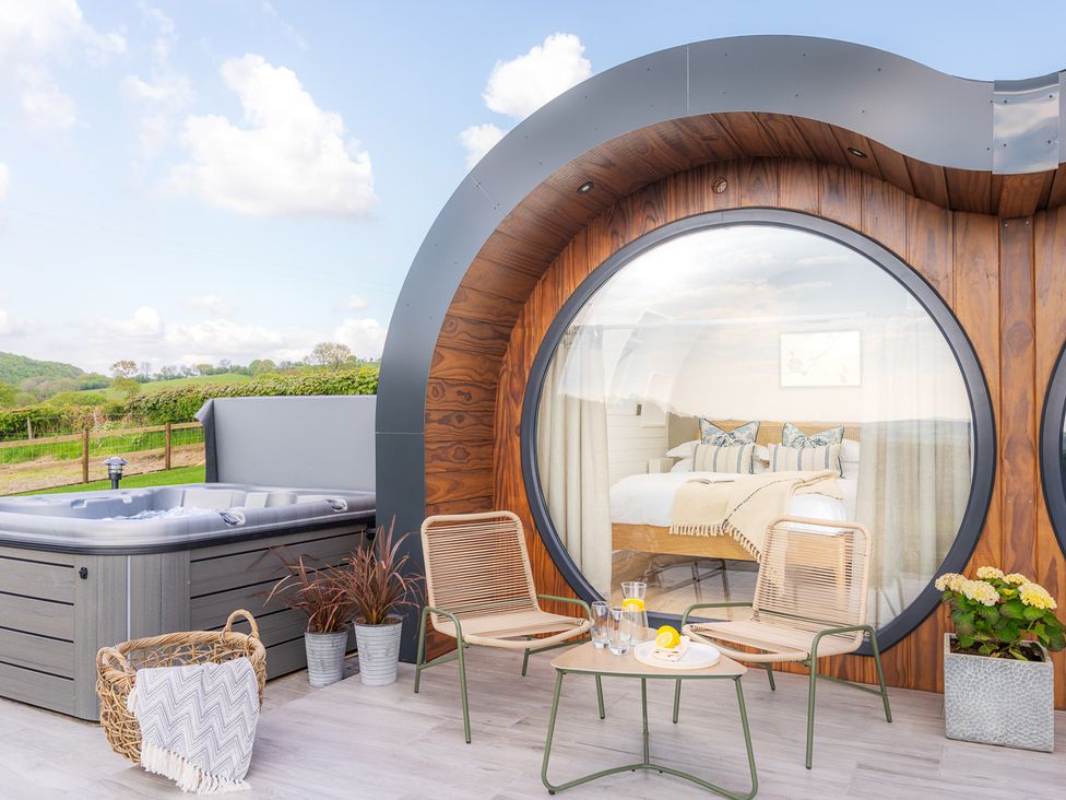 Outdoor patio area with two chairs a table a hot tub and large circular window showing a bedroom at Ceunant in Llanfihangel-y-Creuddyn near Aberystwyth