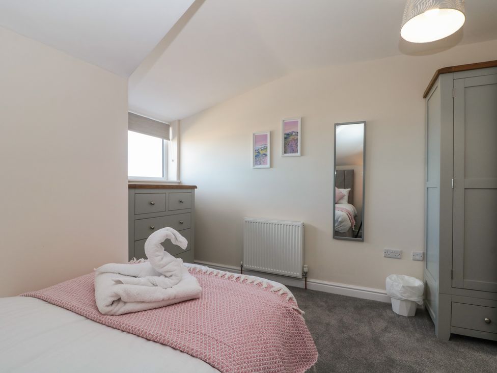 A bedroom with a bed with pink blanket a dresser wardrobe mirror and small trash bin at Seapoint in Primrose Valley