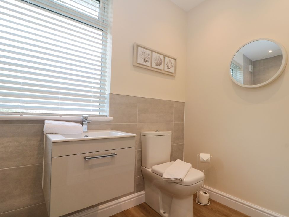 A bathroom with a toilet sink cabinet and round mirror at Seapoint in Primrose Valley
