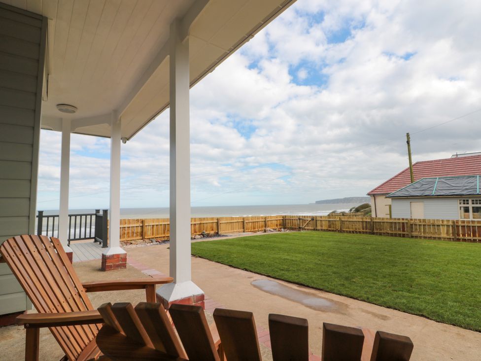 A porch with wooden chairs overlooking a fenced grassy yard and ocean at Seapoint in Primrose Valley