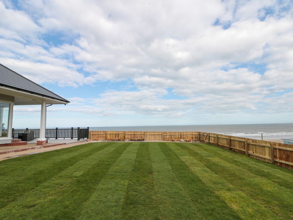 A spacious lawn area with wooden fencing and a patio overlooking the sea at Seapoint in Primrose Valley