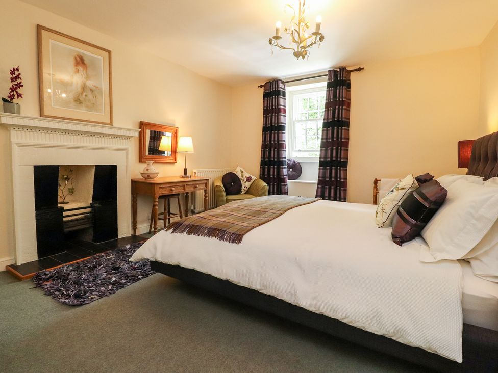 A bedroom with a bed table chair fireplace and window with curtains at Tennant Cottage in Malham
