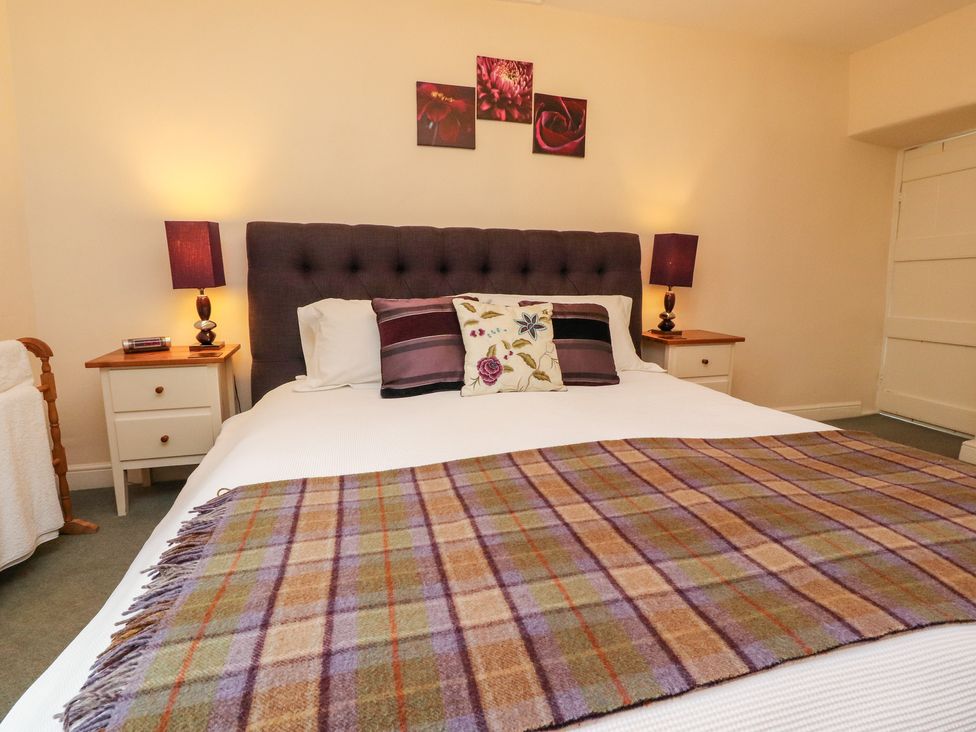 A bedroom with a double bed featuring pillows and a plaid blanket with two bedside tables and lamps at Tennant Cottage in Malham