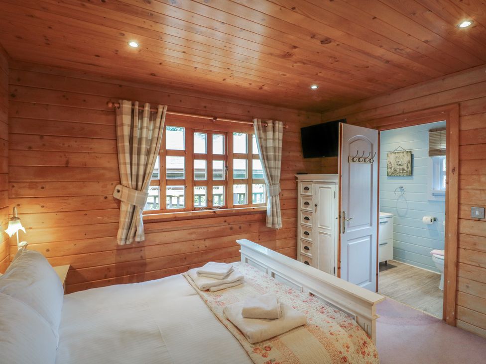 A bedroom with a white bed near a window with checkered curtains and an open door to a bathroom at Pine in Swanage