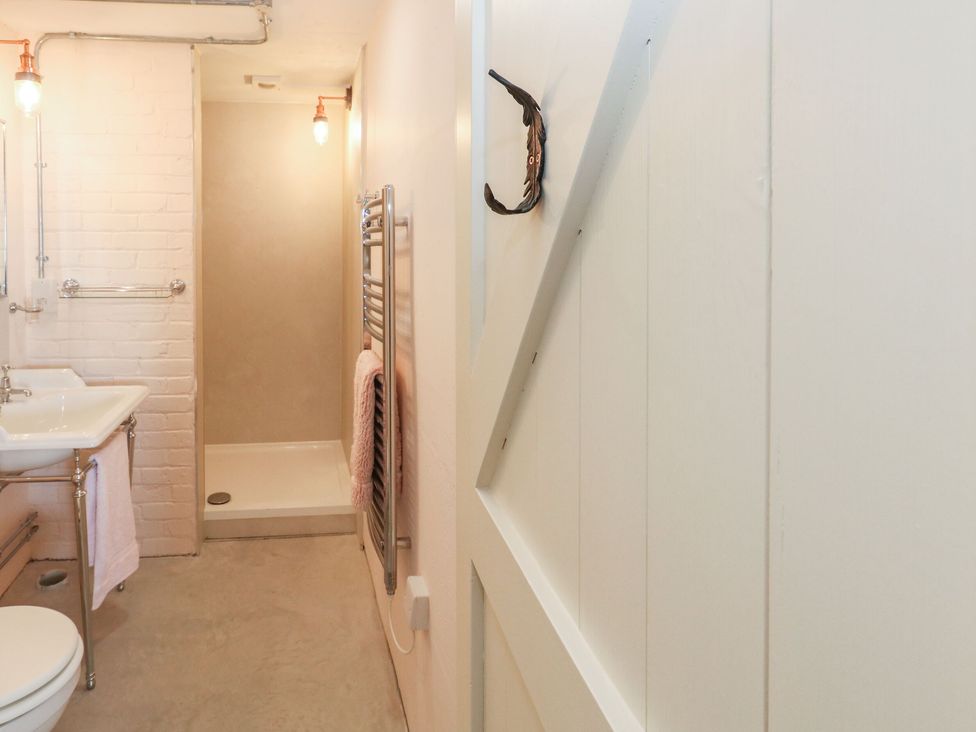 A small bathroom with a shower, sink, toilet, towel rack, and door at The Transmitter Bunker in Ringstead