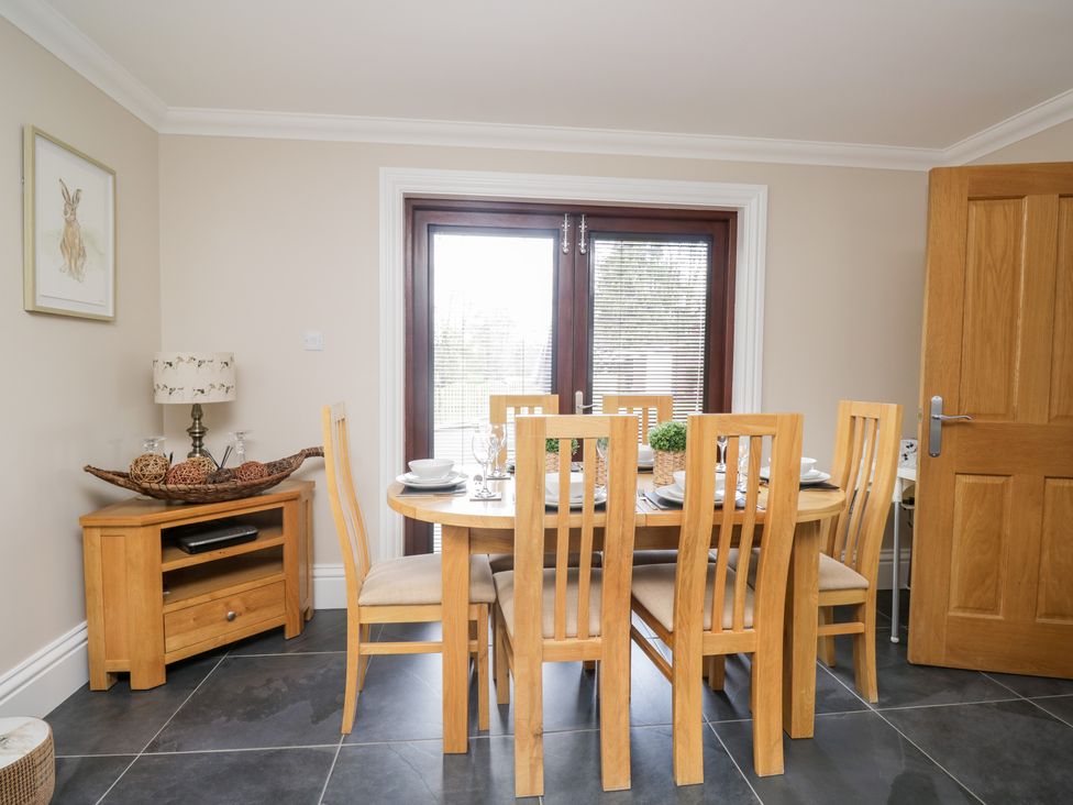 A dining area with a wooden table set for six and a small wooden cabinet with a lamp and decorative items Mill End Eamont Bridge near Penrith