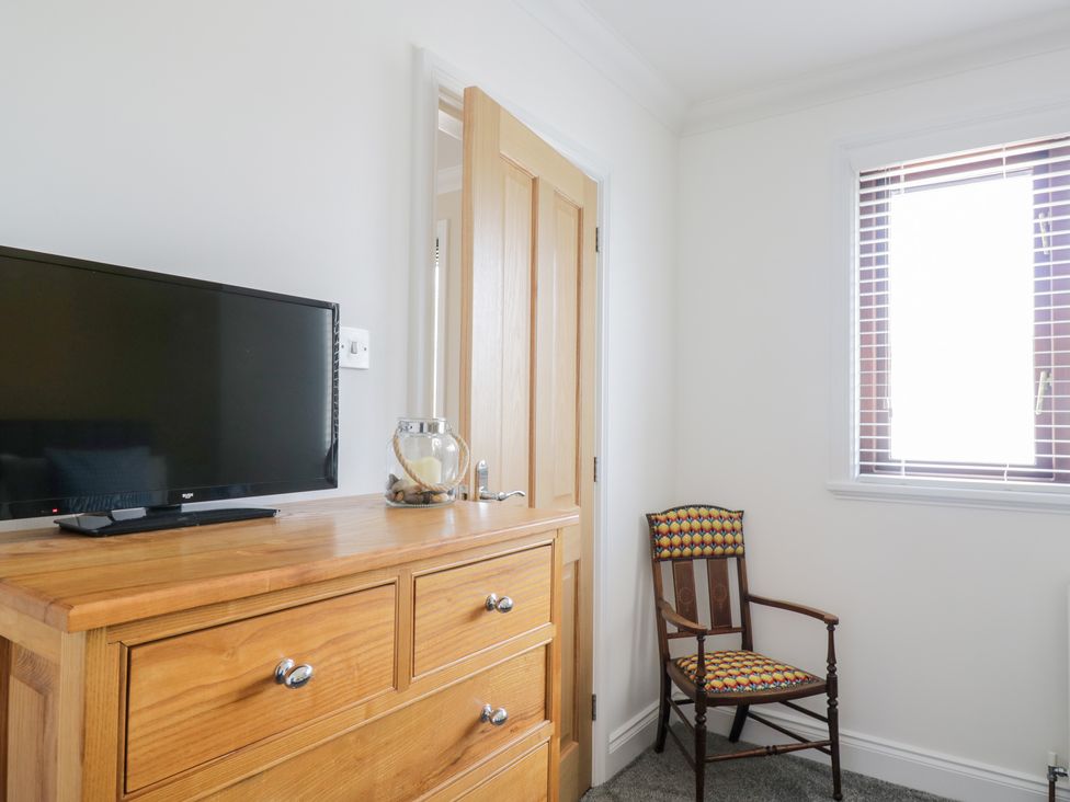A wooden dresser with a TV and glass candle holder next to a wooden door and a patterned chair near a window at Mill End in Eamont Bridge near Penrith
