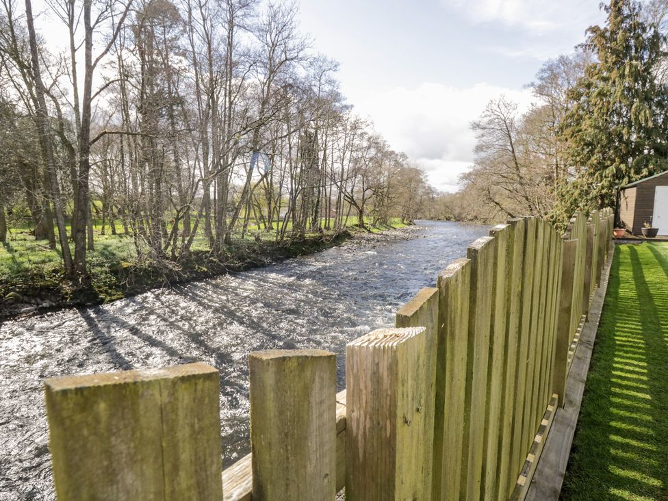 A river with a wooden fence and grass on the right side and trees on the left side at Mill End in Eamont Bridge near Penrith