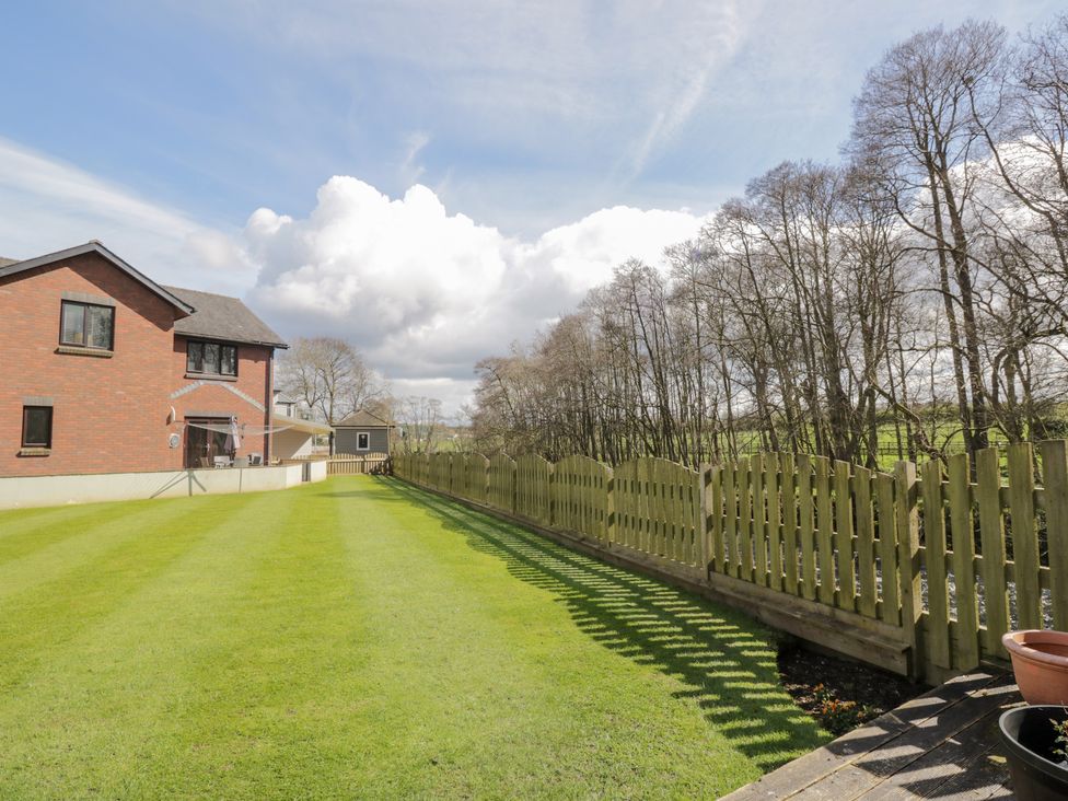 A backyard with a green lawn and a wooden fence next to a brick house at Mill End in Eamont Bridge near Penrith