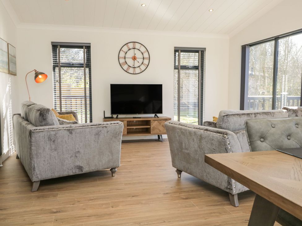 A living room with two gray sofas a wall clock and a television at Watch Tree Lodge in Allithwaite near Cartmel