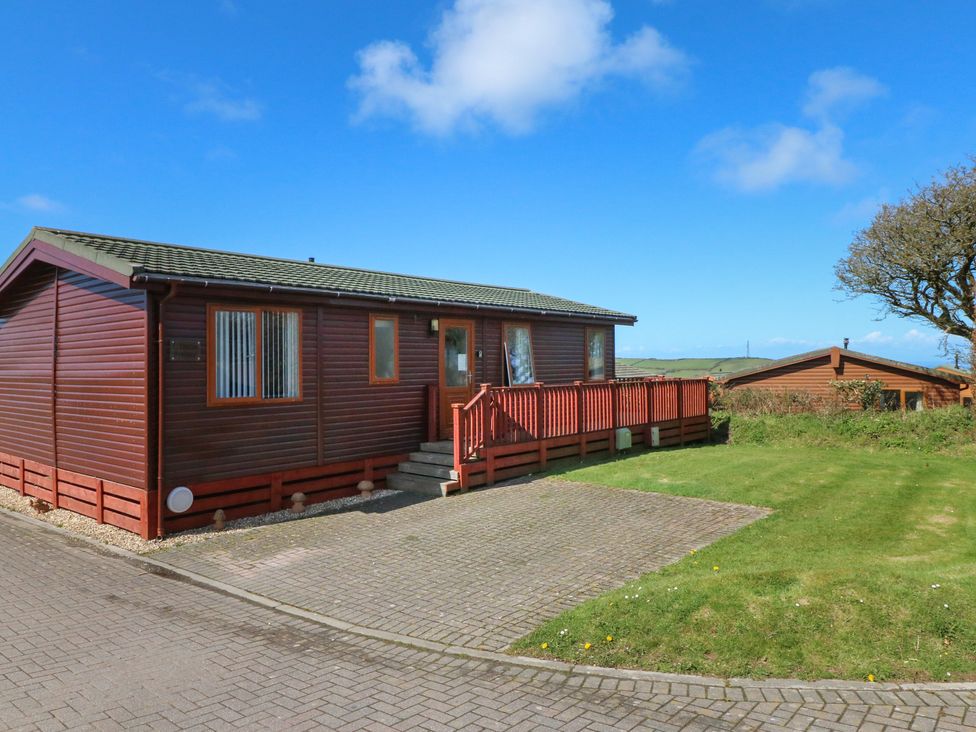 A single story wooden cabin with a small porch and ramp next to a paved driveway and grass at Ocean Terrace 1 Mullacott near Ilfracombe