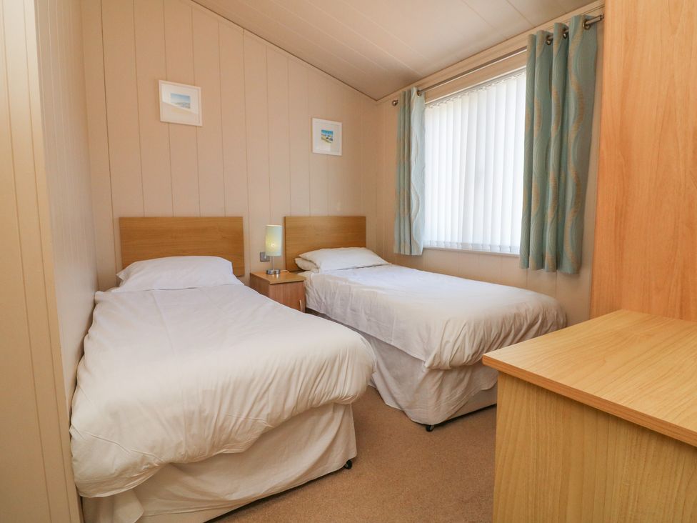 A bedroom with two single beds a nightstand with a lamp a window with curtains and a wooden dresser at Ocean Terrace 1 Mullacott near Ilfracombe