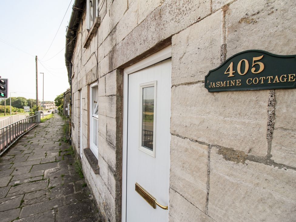 The exterior of a stone building with a white door and a sign reading 405 Jasmine Cottage next to a paved sidewalk