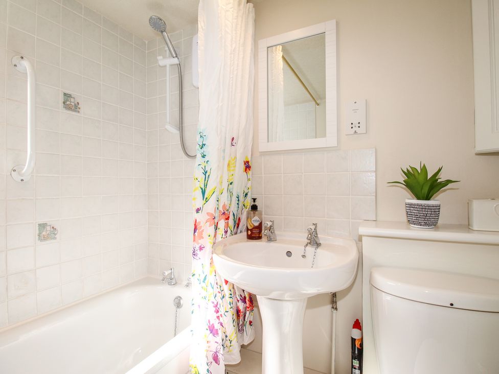 A bathroom with a bathtub shower combination a sink a mirror a toilet and a plant on the toilet unit at Jasmine Cottage in Swanage