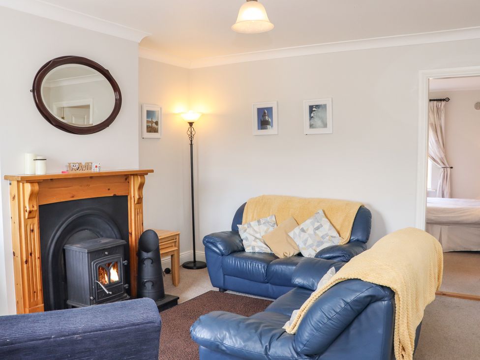 A living room with blue leather sofas yellow throws a fireplace and a floor lamp at South Beach in Duncannon County Wexford