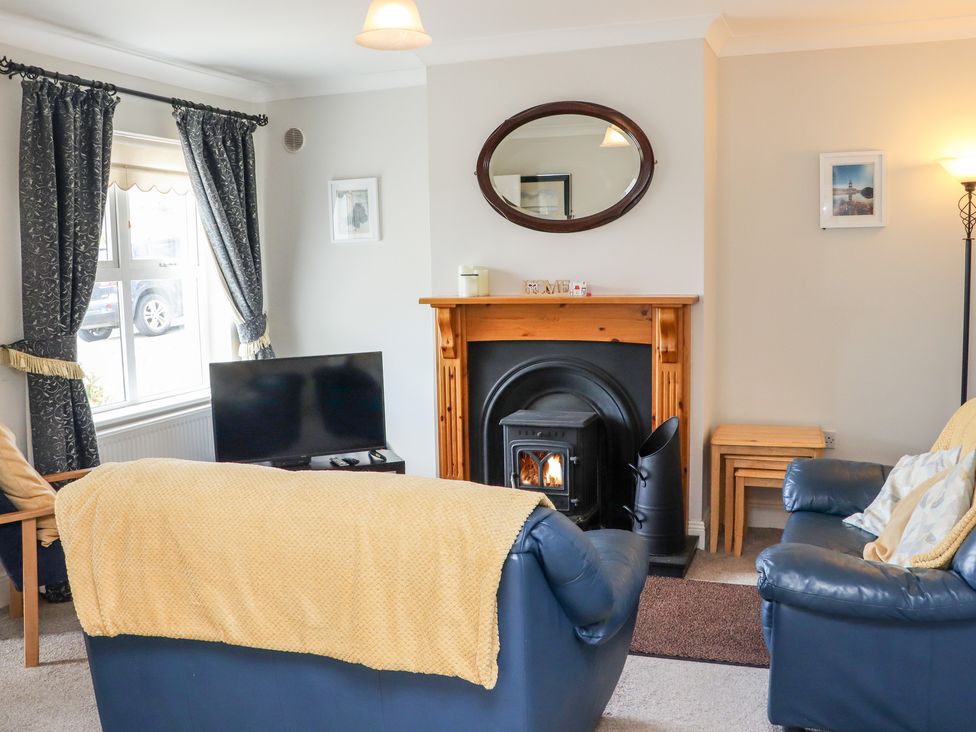 A living room with blue leather sofas a fireplace a television and windows with patterned curtains at South Beach in Duncannon County Wexford
