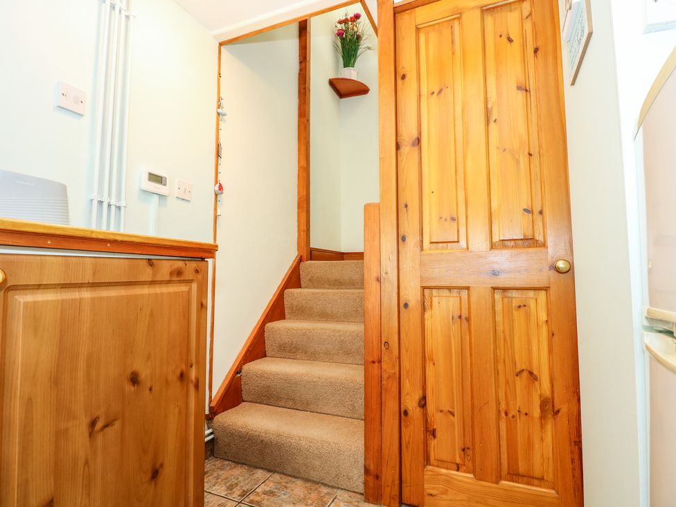 A narrow staircase with beige carpet next to a wooden door and wooden cabinet in a hall at Beck Cottage in Sheringham