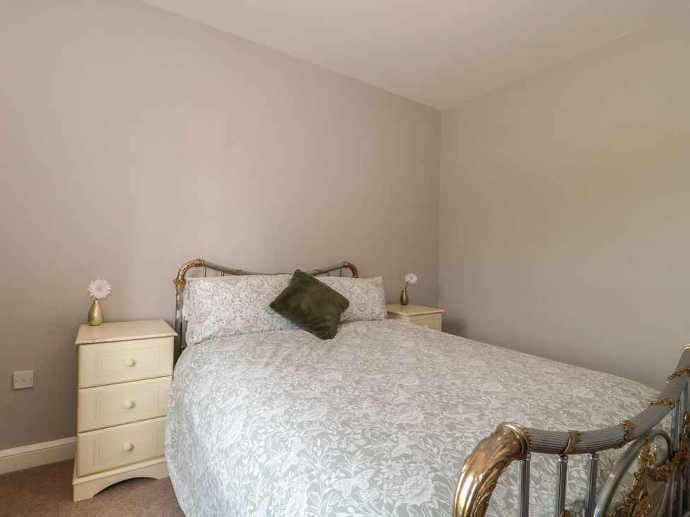 A bedroom with a double bed with floral bedding and two nightstands each with a small vase and flower at Cherry Tree House in Highbridge