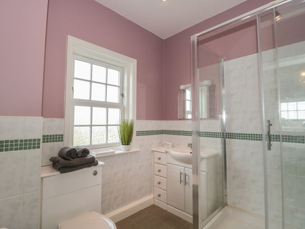 A bathroom with a shower enclosure, sink with cabinet, toilet, a window with frosted glass, towels on the toilet tank, and a plant on the window sill at Cherry Tree House in Highbridge