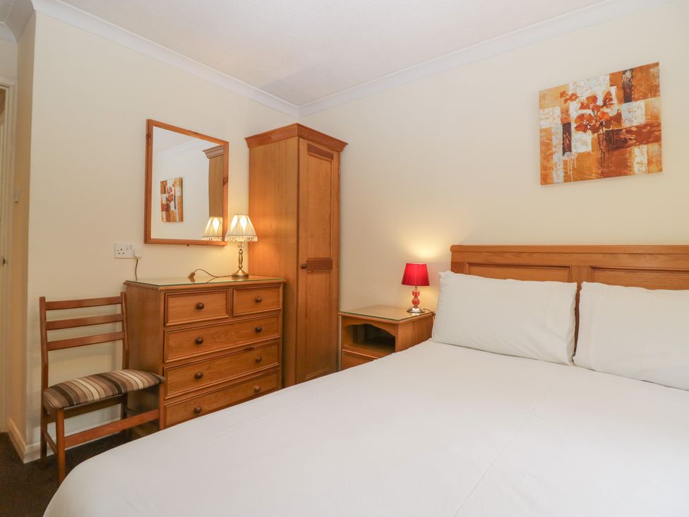 A bedroom with a bed white pillows a wooden dresser a wooden wardrobe a chair and two table lamps at Beech Timber Lodge in Keswick