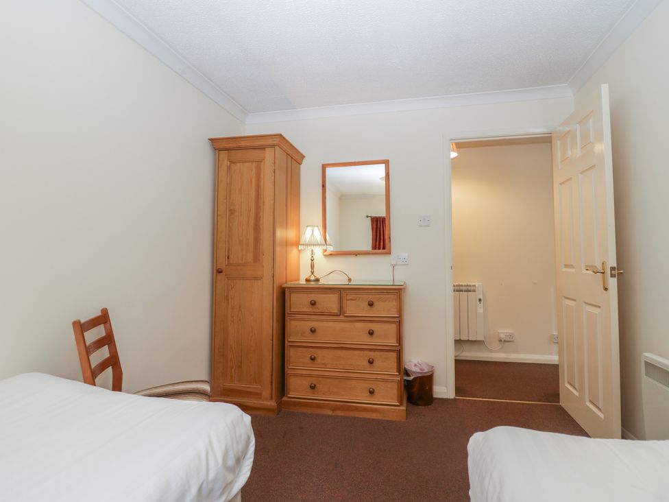 A bedroom with two beds a wooden wardrobe and chest of drawers with a lamp and mirror at Beech Timber Lodge in Keswick