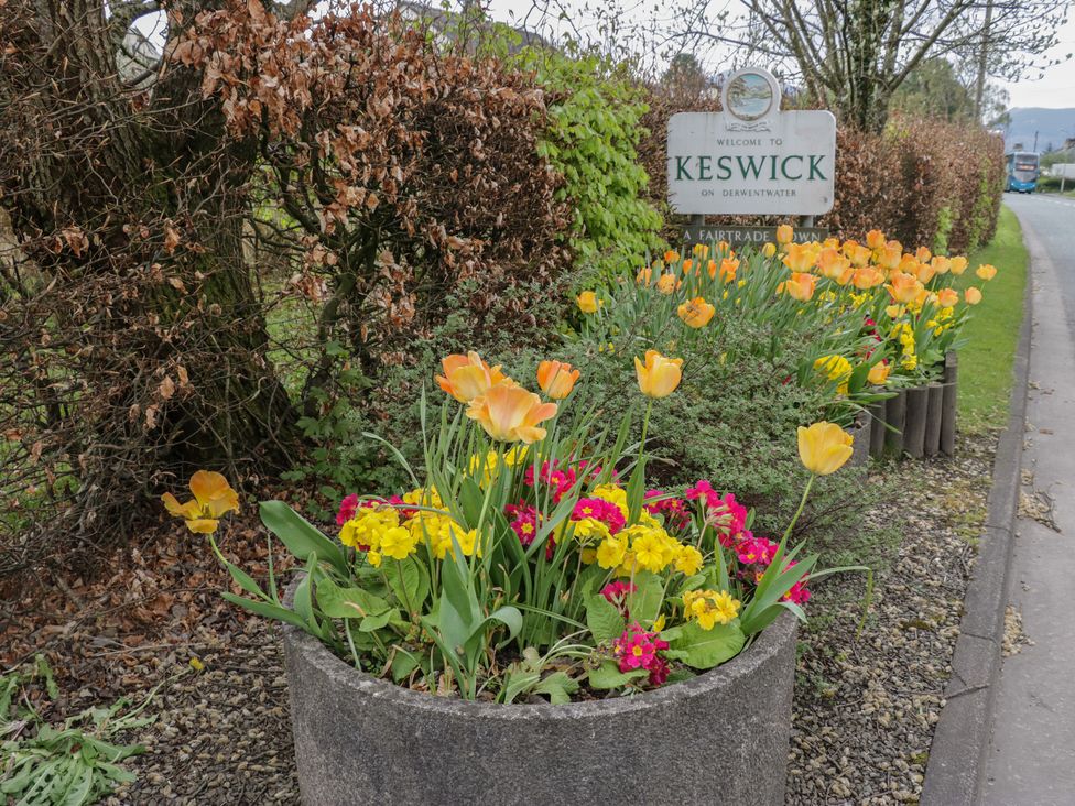A roadside flower planter with yellow and pink flowers near a welcome to Keswick sign at Beech Timber Lodge in Keswick