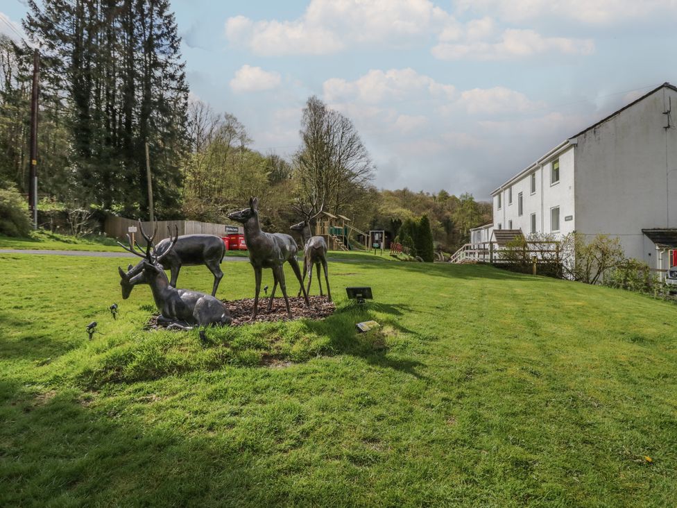 A grassy outdoor area with deer statues near a white building and trees at Beech Timber Lodge in Keswick