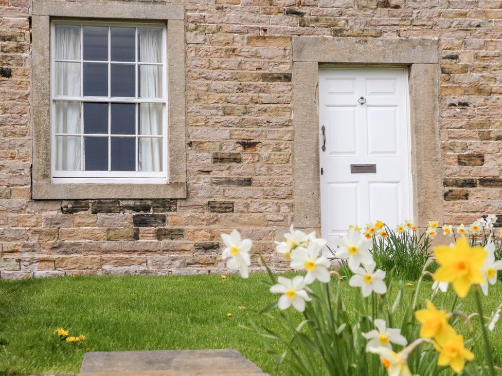 A stone house exterior with a white door and window with white curtains and daffodils in the front garden at Covercote Horsehouse near Leyburn