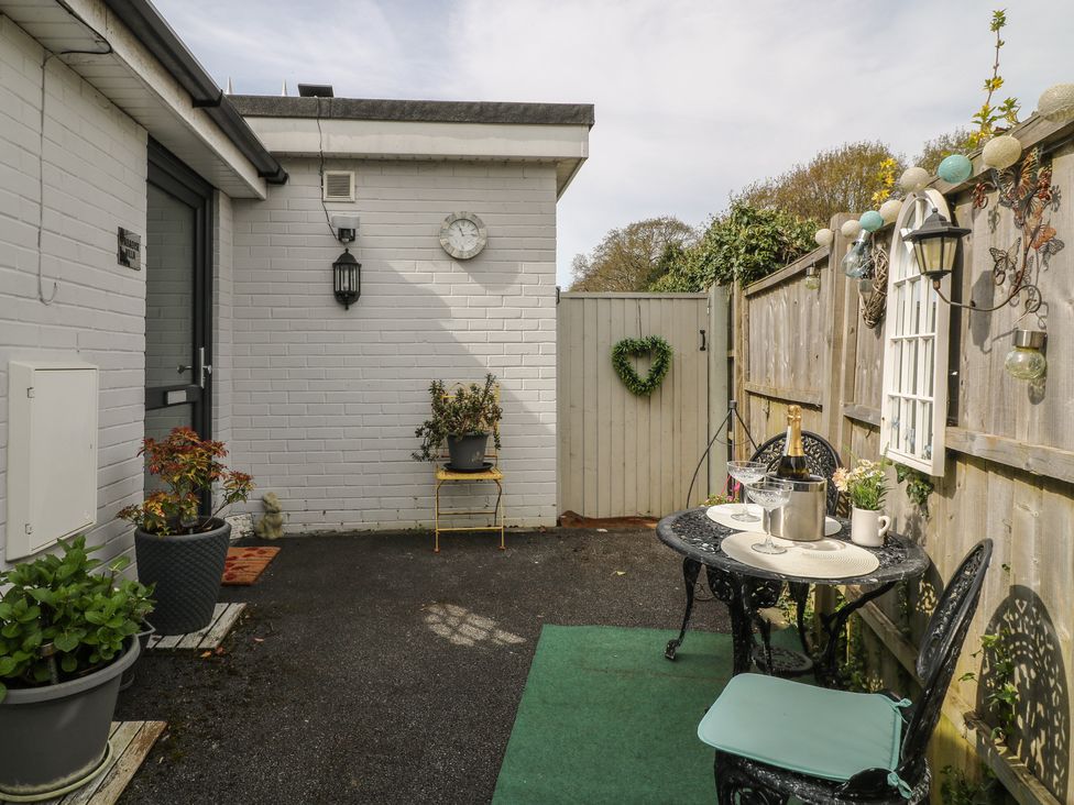 A small outdoor patio with black metal table and chairs a bottle in an ice bucket and potted plants at Paradise Villa in Highcliffe