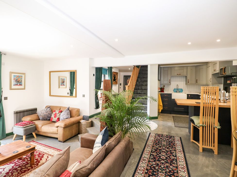 An open living space with sofas coffee table rugs a plant stairs and kitchen at The Masters House in Albourne near Hurstpierpoint