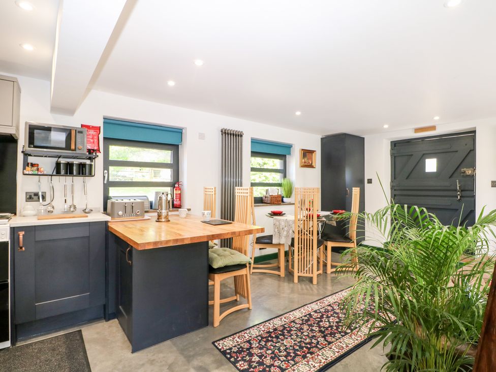 A kitchen and dining area with wooden chairs a wooden countertop a microwave and a patterned rug at The Masters House in Albourne near Hurstpierpoint