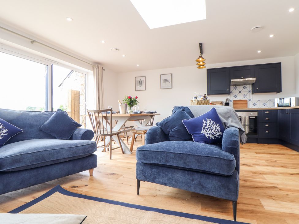 A living room with blue sofas a dining table and chairs and a kitchen with dark cabinets at Chi an Mor in Lower Kenneggy near Praa Sands