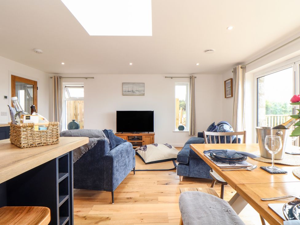A living room with blue sofas a wooden TV stand and a dining area at Chi an Mor in Lower Kenneggy near Praa Sands