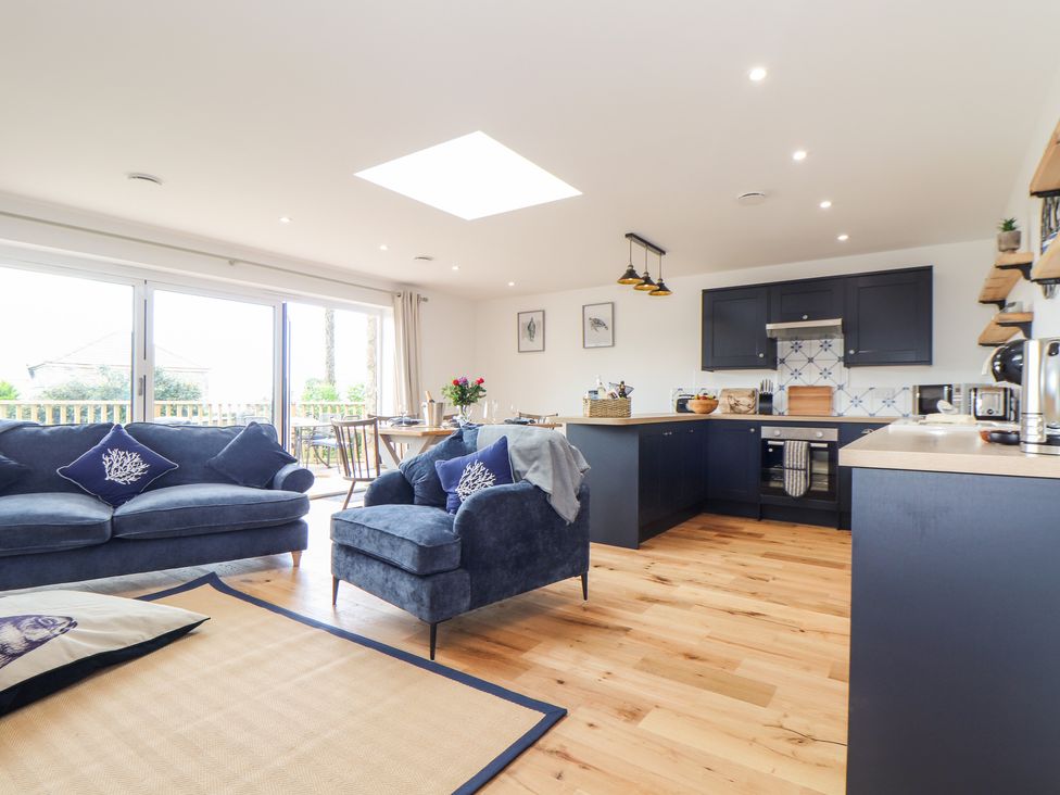 An open plan living room and kitchen with blue sofas wooden floor and dining table at Chi an Mor in Lower Kenneggy near Praa Sands
