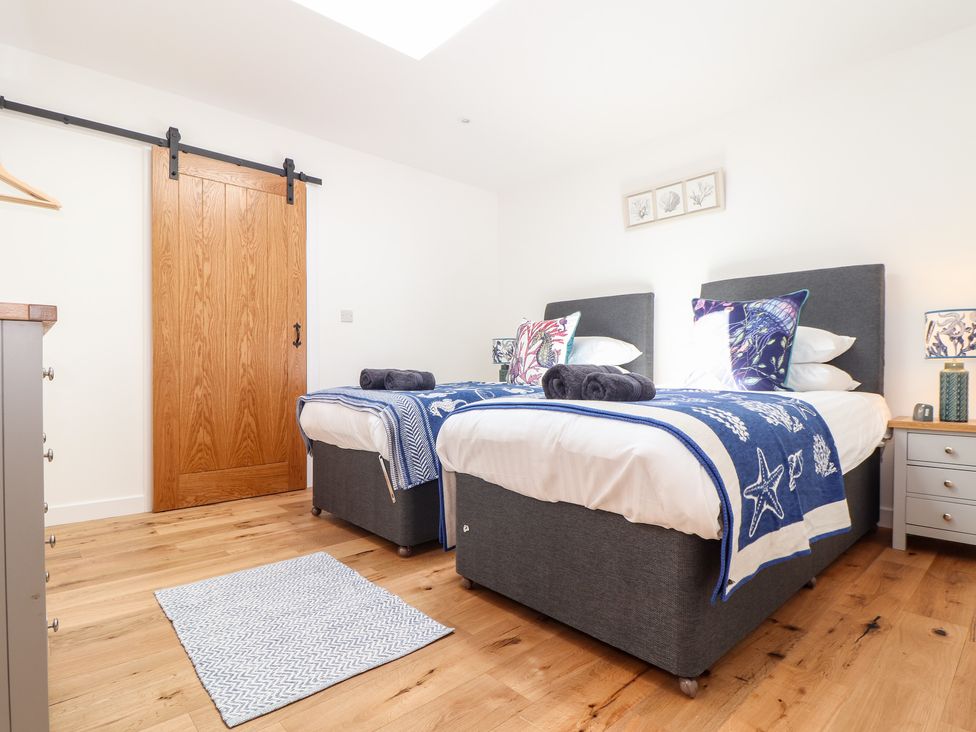 A bedroom with two single beds a wooden floor and a sliding wooden door at Chi an Mor in Lower Kenneggy near Praa Sands