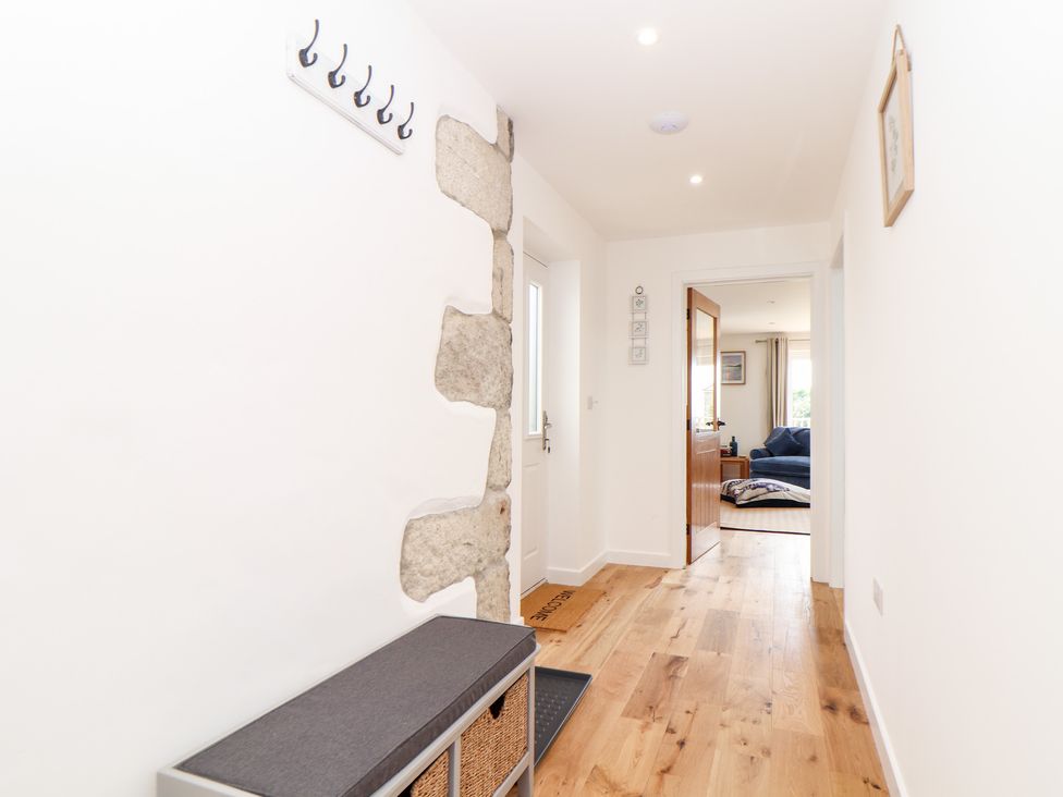 A hallway with wooden floor a bench with baskets wall hooks and a view into a living room at Chi an Mor Lower Kenneggy near Praa Sands