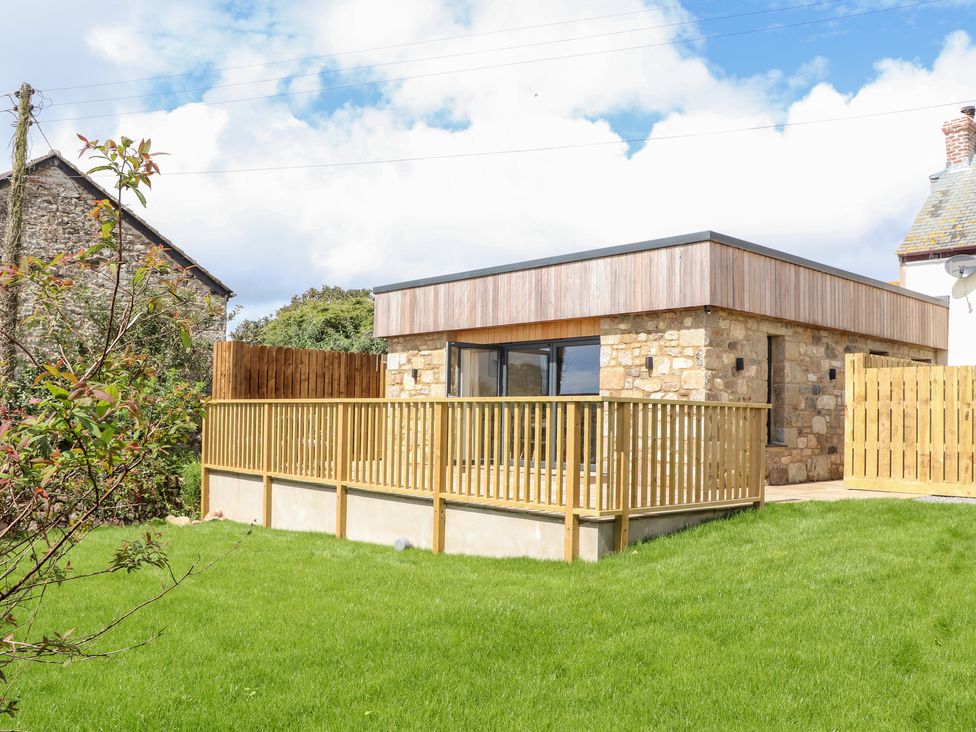 A stone and wood house with a wooden fence and green lawn at Chi an Mor in Lower Kenneggy near Praa Sands
