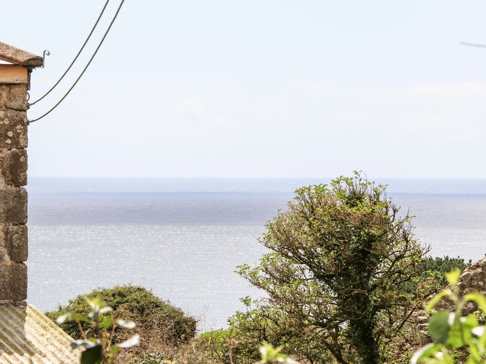 A view of the sea with trees and part of a stone building near Lower Kenneggy near Praa Sands