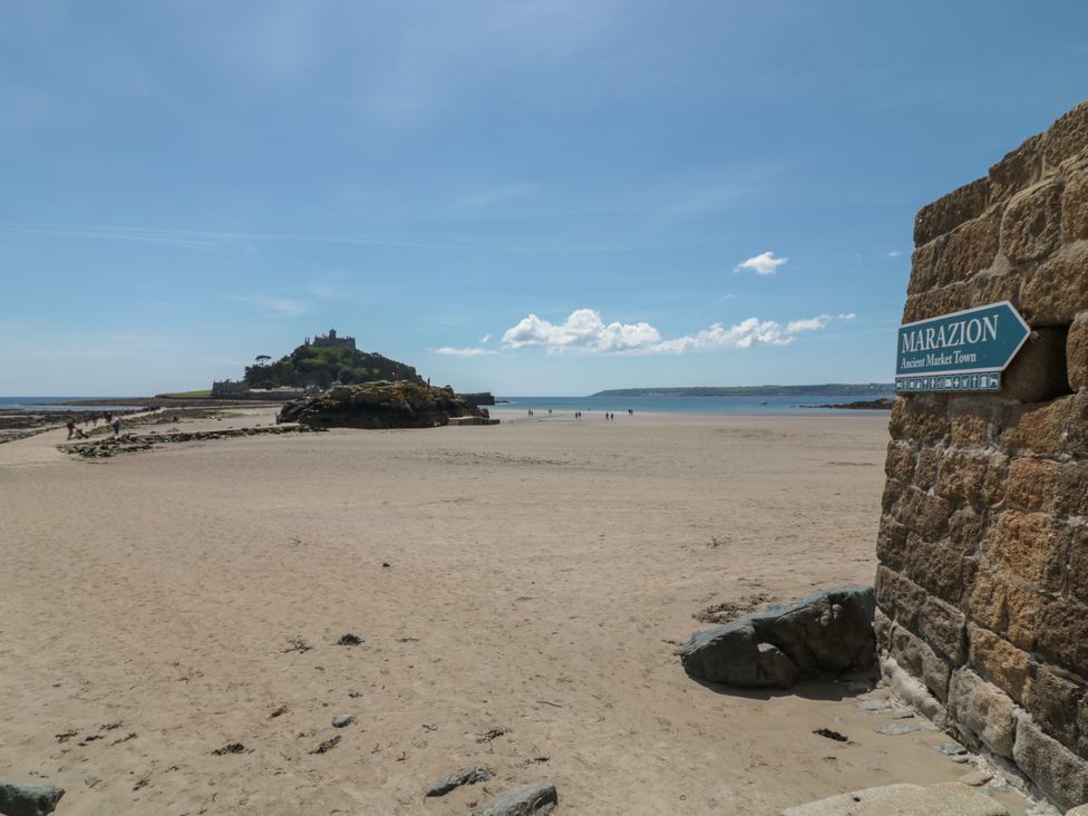A sandy beach with a castle on a hill in the distance and a sign pointing to Marazion Ancient Market Town at Chi an Mor in Lower Kenneggy near Praa Sands