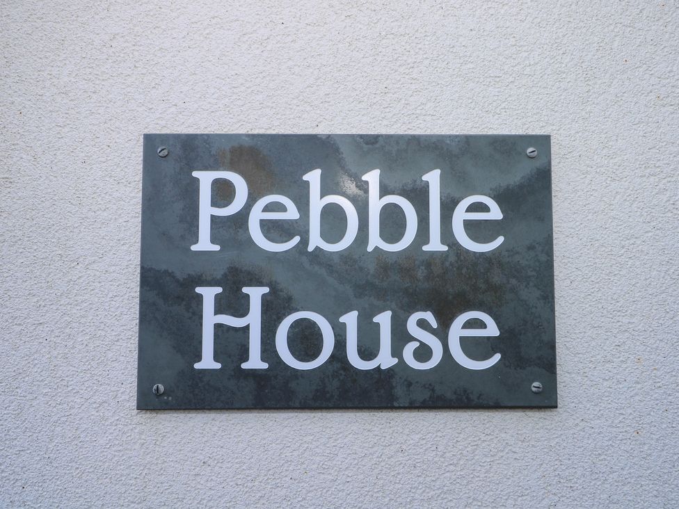 A black metal sign with white text saying Pebble House on a textured white wall at Pebble House in Worthing