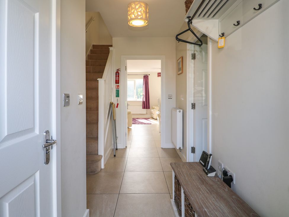 A hallway with tiled floor and stairs leading up with a wooden bench and coat hooks at Pebble House in Worthing