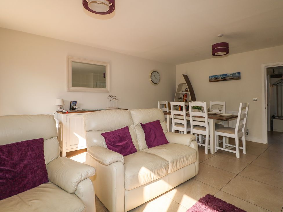 A living room and dining area with cream sofas with purple cushions a wooden dining table with white chairs a mirror on the wall and a wall clock at Pebble House in Worthing