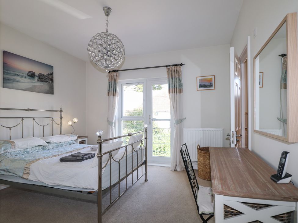 A bedroom with a metal bed frame a wooden desk and chair a wicker basket and a glass door with curtains at Pebble House in Worthing