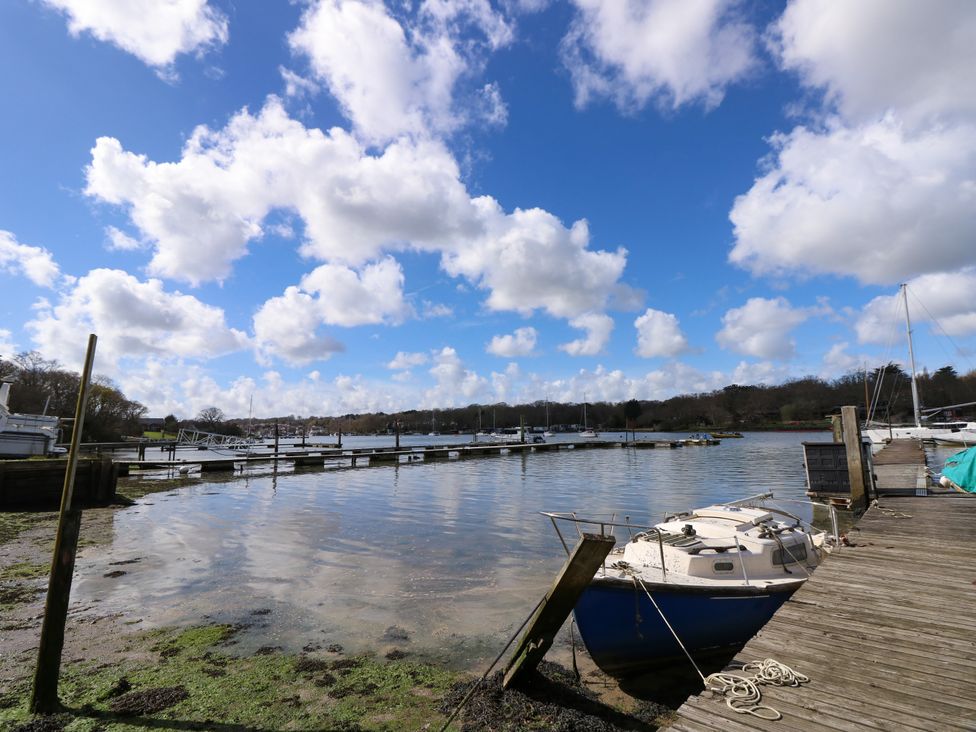 A small boat docked next to a wooden pier on a calm body of water with other boats and docks in the distance at Byewater in Ryde