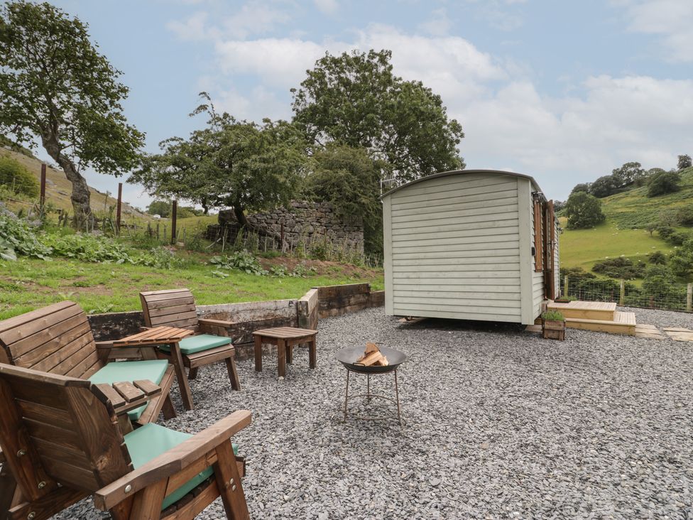 An outdoor seating area with wooden chairs and a fire pit near a small cabin in a rural setting at Tan Y Castell Shepherds Hut in Llangollen
